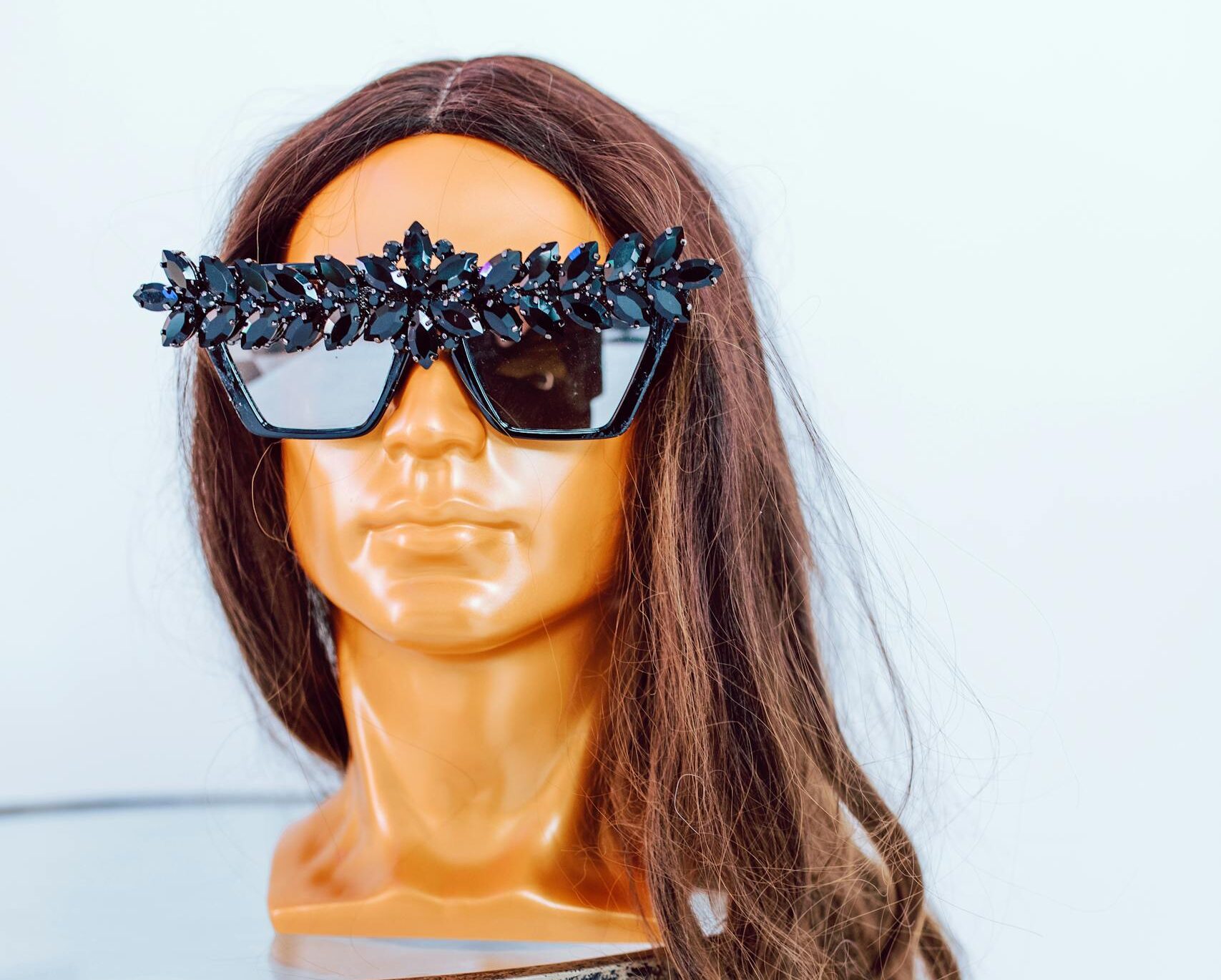 Stylized mannequin head featuring a long wig and embellished sunglasses, showcasing fashion and beauty accessories.